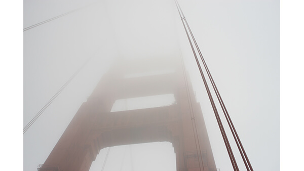 A photograph of a bridge disappearing into fog.