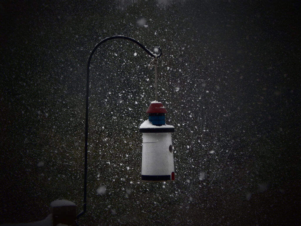 A photograph of a quaint birdhouse surrounded by snowflakes.