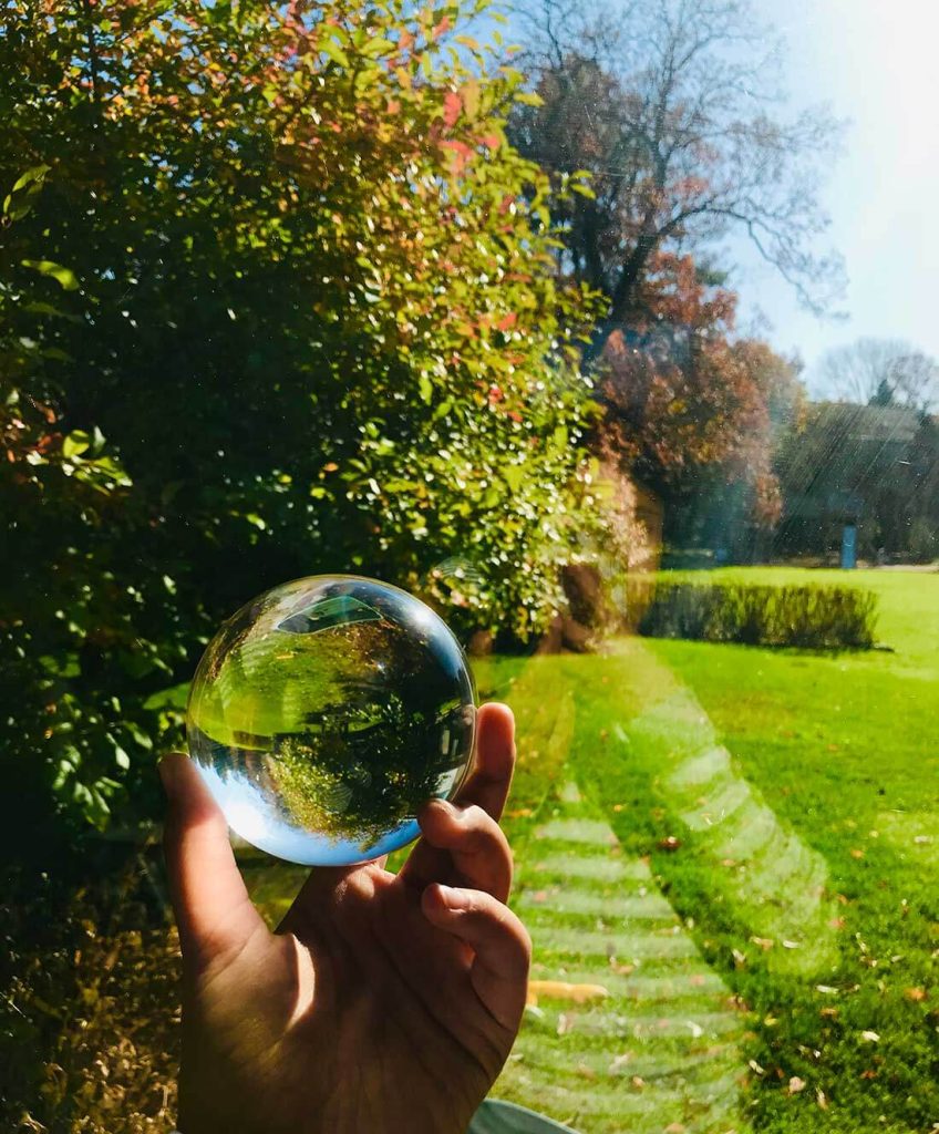 A photograph of a hand holding a glass sphere that reflects the surrounding landscape.