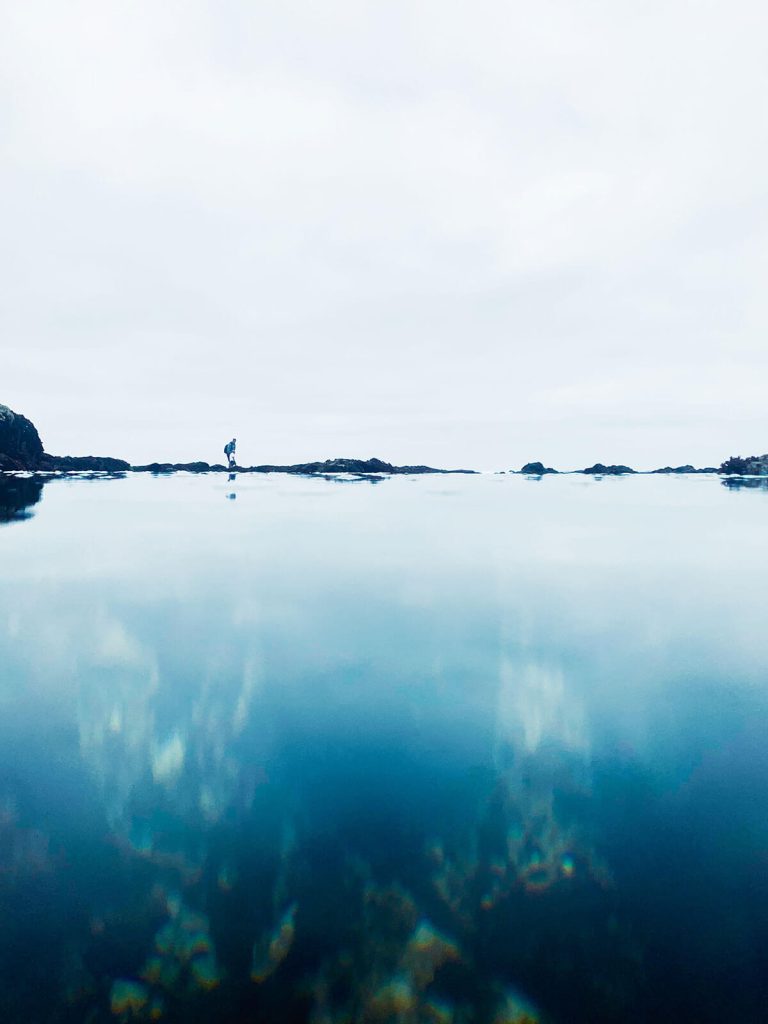 A photograph of a simple ocean landscape, with a person walking between the water and sky.