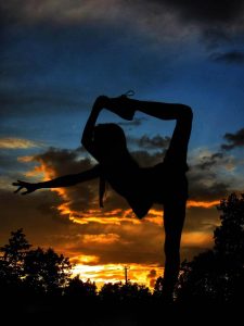 A photograph of a dancer silhouetted against the sunset sky.