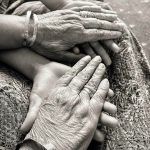 A loving black-and-white photograph of wrinkled hands clasping young ones.